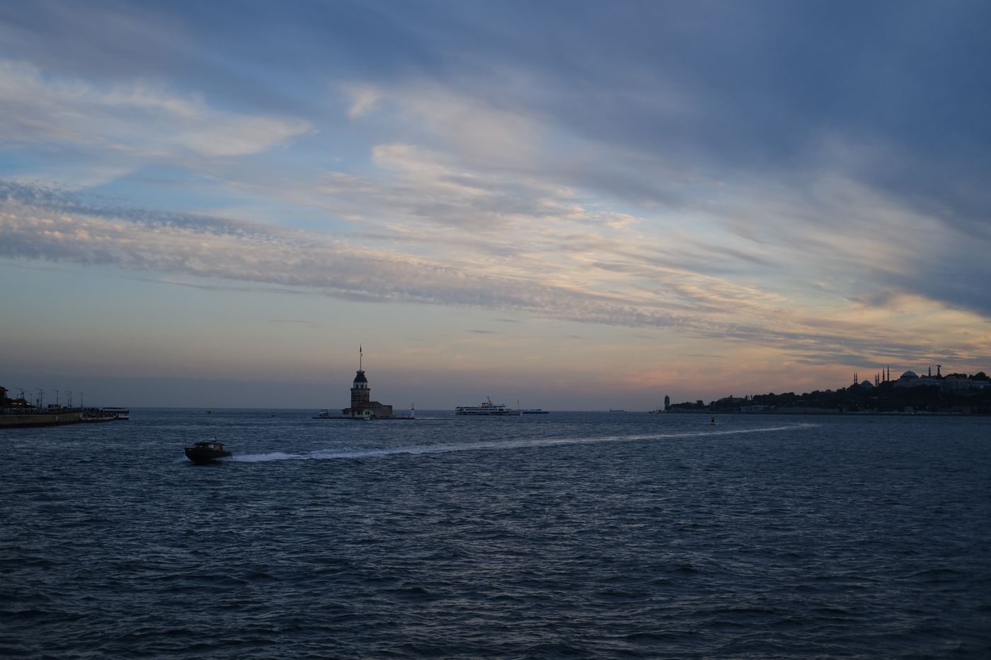 The Maiden's Tower standing in the water at dusk, with the historic Istanbul skyline on the horizon behind it